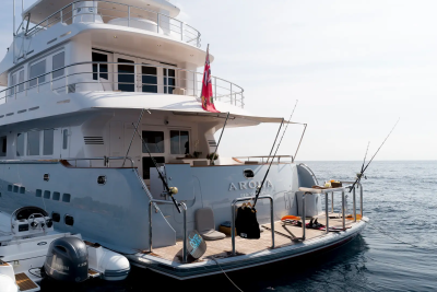 A large white yacht with fishing rods on its deck floats on calm blue water under a bright sky.