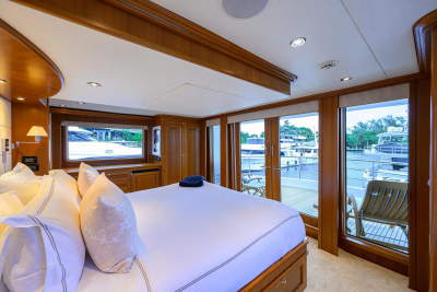 A luxurious bedroom with a large bed in the foreground and a view of a marina with boats in the background through large windows.