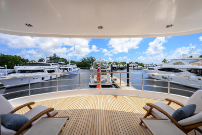 Two lounge chairs on a wooden deck overlook a marina filled with yachts under a bright blue sky.