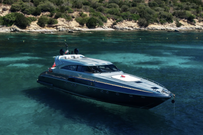 A sleek, modern yacht floats on clear turquoise water in the foreground, with a lush, green hillside rising in the background.
