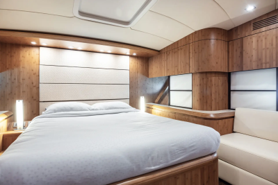 A luxurious bedroom with a white-sheeted bed in the foreground and wood-paneled walls and a white sofa in the background.