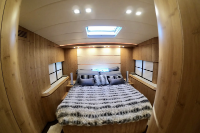 A luxurious bedroom with a plush bed in the foreground and wood-paneled walls and a skylight in the background.