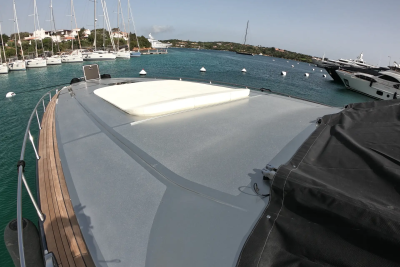 A white hatch sits on the grey deck of a boat in the foreground, with sailboats and yachts docked in the turquoise water of the background.
