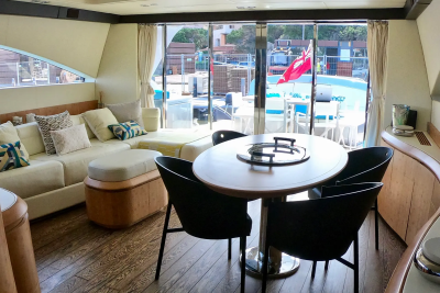 A circular dining table with four chairs sits in the foreground, while a plush sectional sofa and large windows overlooking a sunny marina fill the background.