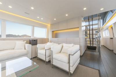 Modern white armchairs and a sofa in the foreground face a large window with a mountain view in the background, while a sleek staircase leads to another level.