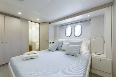 A neatly made bed with striped bedding and decorative pillows sits in the foreground, while two porthole windows are visible in the background above the headboard.
