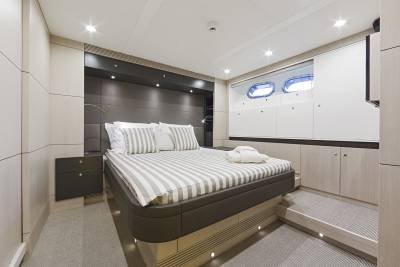 A luxurious bedroom with a king-sized bed in the foreground and a wall of white cabinets with porthole windows in the background.