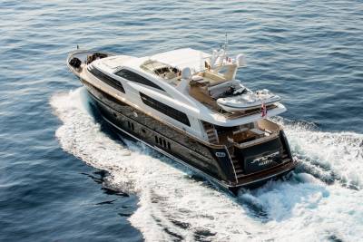 A luxurious dark-hulled yacht cruises through calm blue water, leaving a white wake behind it, with a clear sky above.