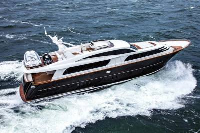 A sleek, dark-hulled yacht with a wooden deck cuts through choppy, dark blue water, leaving a white wake behind it.