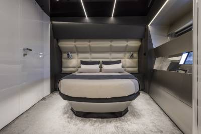 A modern, futuristic bedroom with a plush, tufted headboard and a sleek, elevated bed in the foreground, set against a backdrop of minimalist white walls and integrated lighting.