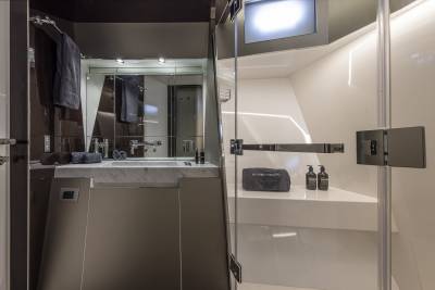 A modern bathroom with a sleek vanity and sink in the foreground, and a glass-enclosed shower with toiletries in the background.