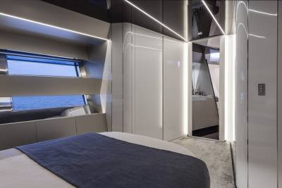 A modern bedroom with a blue-covered bed in the foreground and a sleek, illuminated bathroom visible in the background through an open doorway.