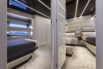 A modern yacht cabin with two beds in the foreground and a view of the sea through windows in the background.