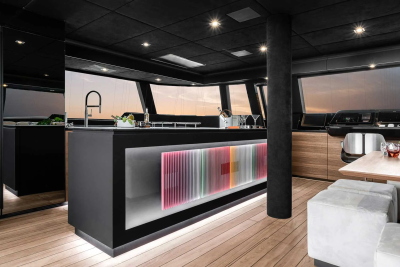 A modern, sleek kitchen with a black island illuminated by colorful lights in the foreground, and large windows offering a sunset view in the background.