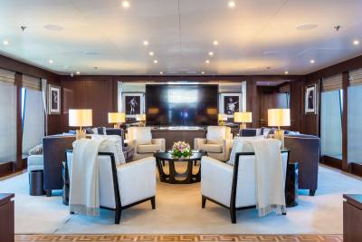 Plush armchairs with draped throws face a large television screen in a luxurious lounge, while framed artwork adorns the dark wood paneled walls in the background.