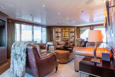 Plush leather armchairs and a fur throw are in the foreground, while a well-stocked display cabinet and large windows fill the background of this luxurious lounge.