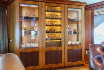 A wooden cabinet filled with bottles and cigars stands in front of a window overlooking the water.