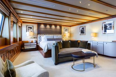 A luxurious yacht bedroom with a plush sofa and ottoman in the foreground and a large bed with a tufted headboard in the background.