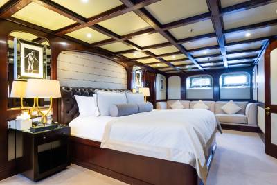 A luxurious bedroom with a large bed in the foreground and a plush sofa and windows in the background, all under a coffered ceiling.