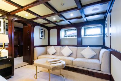 A plush sofa with decorative pillows and a small ottoman sit in the foreground of a room with dark wood paneling and arched windows in the background.