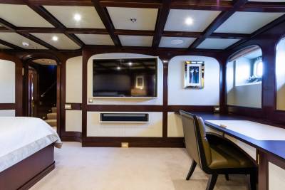 A luxurious bedroom with a large bed in the foreground and a desk with a television and a window in the background.