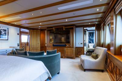 A luxurious yacht cabin features a plush sofa and armchair in the foreground, with a large television and wooden cabinetry in the background.