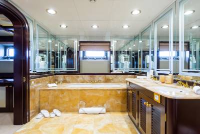 A luxurious bathroom with a marble bathtub in the foreground and mirrored cabinets reflecting the windows in the background.