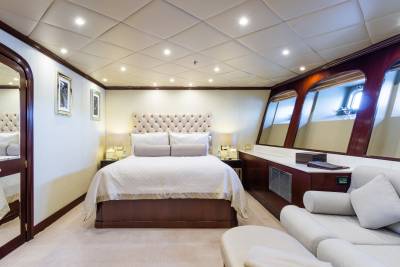 A luxurious yacht cabin features a tufted headboard bed in the foreground and large windows with a view of the sea in the background.