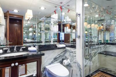 A luxurious bathroom with a marble-clad toilet and shower in the foreground, and a mirrored wall reflecting toiletries and lighting in the background.