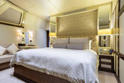 A luxurious bedroom with a large bed in the foreground and a vanity area with a sofa in the background.