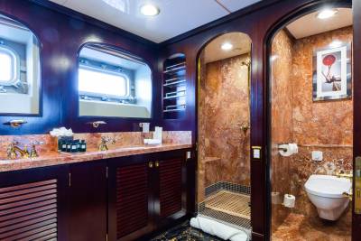 A luxurious bathroom with a marble vanity and sinks in the foreground, and a marble shower and toilet in the background.