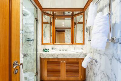 A luxurious bathroom with a marble vanity and a glass-enclosed shower in the foreground, and a triptych mirror reflecting the wood-paneled interior in the background.