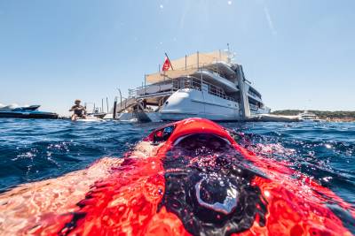 A red paddleboard floats in the foreground with a large white yacht and a person on a jet ski in the background.