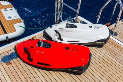 Two personal watercraft, one red and one white, rest on a wooden deck beside a boat in the blue ocean.