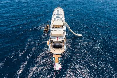 A large white yacht with a slide and a tender boat is anchored in the deep blue ocean.