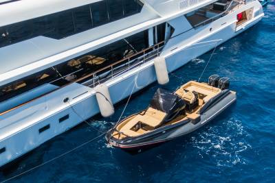 A sleek, modern tender boat is tethered to a large, luxurious yacht floating on a clear blue ocean.