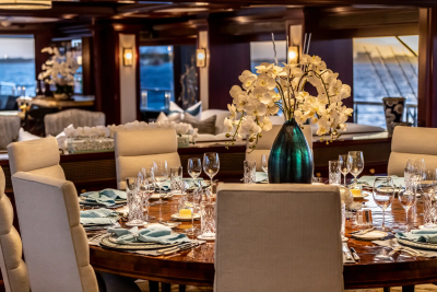 A formal dining table set with elegant place settings and a floral centerpiece is in the foreground, while a luxurious lounge area with comfortable seating and ambient lighting is visible in the background.