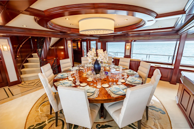 A formal dining table set for a meal is in the foreground, while a panoramic view of the ocean is visible through the windows in the background.
