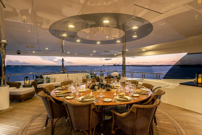 A beautifully set dining table on a yacht's deck overlooks a serene ocean sunset.