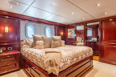 A luxurious yacht bedroom features a large bed with patterned bedding in the foreground, while the background reveals mirrored closets and a glimpse into an ensuite bathroom.