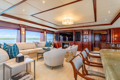 A luxurious yacht interior with a plush sofa and bar in the foreground, and a scenic ocean view through large windows in the background.