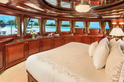A luxurious bedroom with a large bed in the foreground overlooks a tropical ocean view through large windows in the background.