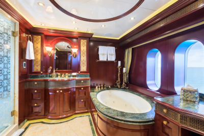 A luxurious yacht bathroom features a large oval bathtub in the foreground and oval windows with a blue sky in the background.