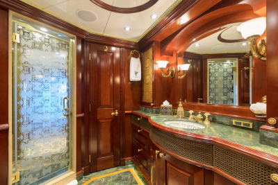 A luxurious yacht bathroom features a frosted glass shower stall in the foreground and a marble-topped vanity with ornate fixtures in the background.