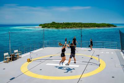 A couple plays pickleball on a helipad with a tropical island in the background.