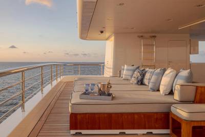 Sun loungers with pillows and drinks are arranged on a yacht's deck, overlooking the ocean at sunset.