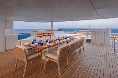 A long dining table set for a meal on a yacht's deck overlooks the ocean.