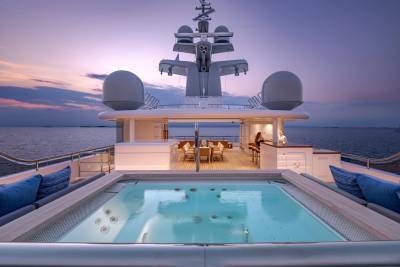 A luxurious yacht's jacuzzi and outdoor dining area are set against a serene ocean sunset.