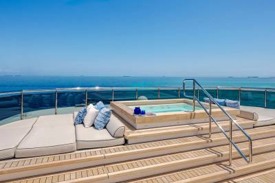 A luxurious yacht's deck features a hot tub and lounge chairs in the foreground, with a vast blue ocean and clear sky in the background.