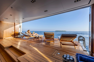 A woman relaxes on a lounge chair on a wooden deck with the ocean and a distant island in the background.